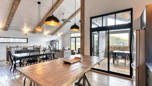 A spacious kitchen with a large wooden table, hanging pendant lights, and a sliding glass door leading to an outdoor deck.