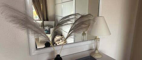A white dresser with a mirror above it, a lamp, and decorative feathers.