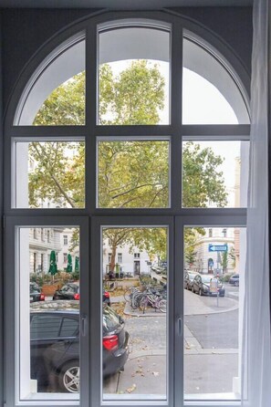 Blick durch ein Fenster auf eine belebte Straße mit parkenden Autos und Fahrrädern.