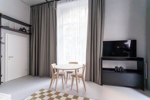 Une chambre moderne avec une table à manger, des chaises, un téléviseur posé sur une étagère et une armoire.