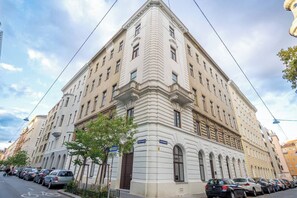 Ein mehrstöckiges Gebäude im klassischen Stil mit Hauseingang an einer Ecke, einer gut sichtbaren Tür und einem Schild, das auf ein Geschäft oder eine Dienstleistung im Erdgeschoss hinweist.
