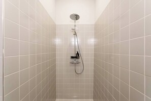 Ein Badezimmer mit weiß gefliesten Wänden, einer Duschbrause und einem Handbrausehalter.