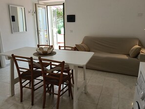 Un coin repas avec une table blanche, quatre chaises en bois, un panier en osier et un canapé beige.