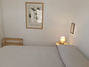 Un dormitorio con cama, una obra de arte enmarcada, una mesita de noche con lámpara y un banco de madera.