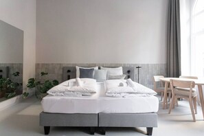 Ein modernes Hotelzimmer mit einem großen Bett, einem kleinen Tisch, Stühlen und Blick auf die Stadt durch das Fenster.