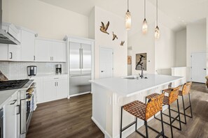 Eine moderne Küche mit weißen Schränken, einer großen Kochinsel mit Barhocker und dekorativer Wandgestaltung.