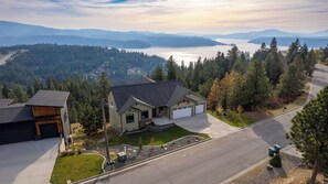 A residential house with a garage, driveway, and a view of a lake and mountains. - Mountaintop Haven: Lakefront 5-Bedroom Lodge for Large Groups (Coeur d'Alene)