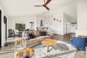 A spacious living area with a large sofa, a coffee table, and a ceiling fan. - Mountaintop Haven: Lakefront 5-Bedroom Lodge for Large Groups (Coeur d'Alene)
