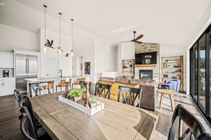 A modern kitchen with white cabinets, a dining area with a wooden table, and a living space with a fireplace. - Mountaintop Haven: Lakefront 5-Bedroom Lodge for Large Groups (Coeur d'Alene)
