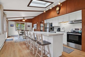 A modern kitchen with wooden cabinets, a central island with bar stools, a stainless steel refrigerator, and a built-in oven.