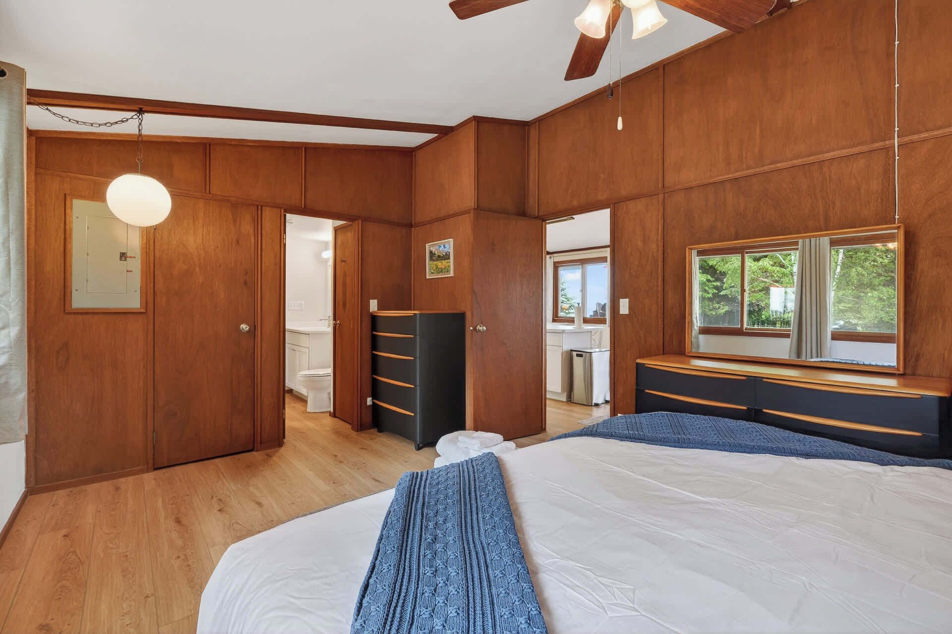 Un dormitorio con cama, cómoda, armario, ventilador de techo y ventana con vista a zonas verdes.