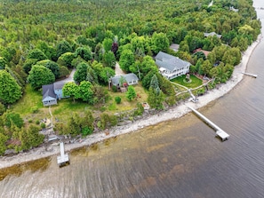 An aerial view of a lakeside property with multiple houses, a dock, and a forested area.