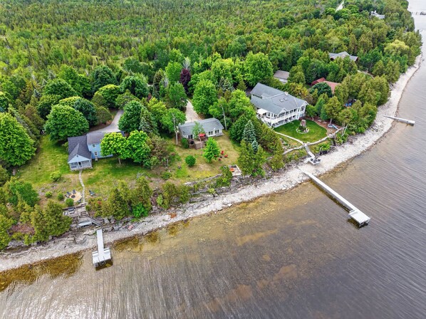 An aerial view of a lakeside property with multiple houses, a dock, and a forested area.