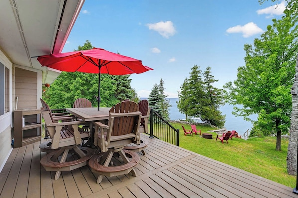 A wooden deck with a table and chairs, a red umbrella, and a view of a lake.