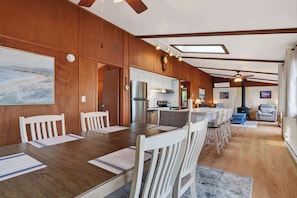 A spacious dining area with wooden paneling, a kitchen in the background, and a cozy seating area with a fireplace.