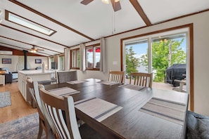 A spacious dining area with a large wooden table, multiple chairs, and a view of the outdoors through large windows.