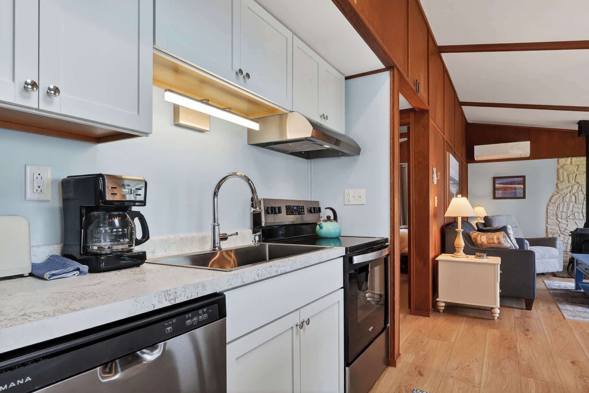A modern kitchen with white cabinets, a coffee maker, a kettle, and a dishwasher.