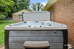 Ein Whirlpool mit einer hölzernen Sitzbank davor, einer Ziegelwand rechts und einem Haus im Hintergrund.