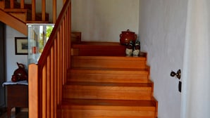 A wooden staircase with a red handrail, leading to a landing with a red pot and a small statue.