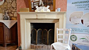 A fireplace with a white mantel, a chair, and a poster advertising agriturismo accommodations.