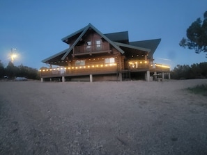 A large wooden building with a balcony, a covered porch, and a gravel driveway.