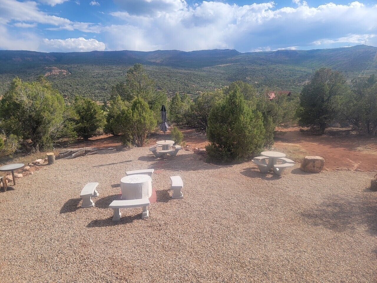 An outdoor seating area with tables and benches, surrounded by trees and a view of distant mountains.