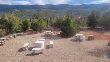 An outdoor seating area with tables and benches, surrounded by trees and a view of distant mountains.