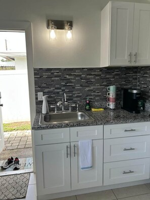 Eine Küche mit Granit Arbeitsplatte, Edelstahlspüle, weißen Schränken und einer Rückwand mit schwarzen Fliesen.