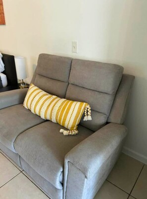 Ein graues Sofa mit einem gestreiften Kissen und einer kleinen, weißen Lampe auf einem Beistelltisch.