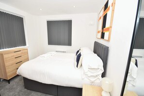 Ein modernes Hotelzimmer mit einem großen Bett, einem Holzschrank, einem Nachttisch mit Lampe und einem Fenster mit Jalousien.