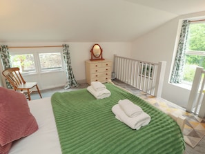 Ein Schlafzimmer mit Bett, Schminktisch, Stuhl, Fenster und Blick auf Grünfläche.