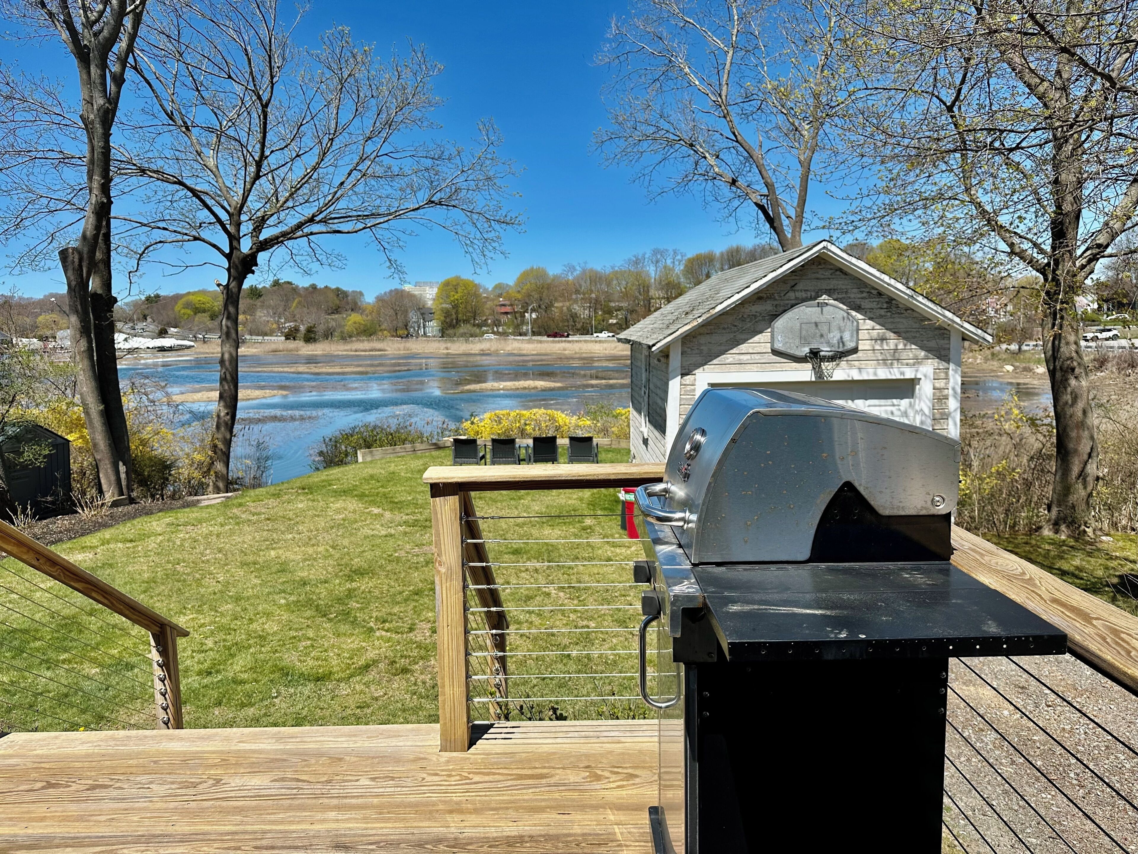 A wooden deck with a barbecue grill, a basketball hoop, and a view of a river and trees.