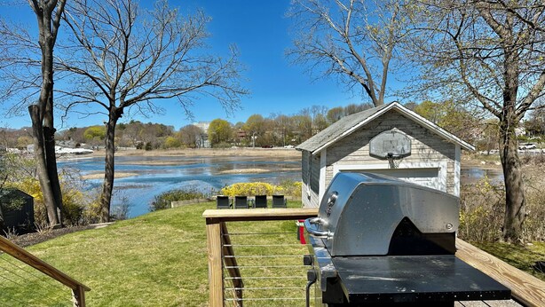 A wooden deck with a barbecue grill, a basketball hoop, and a view of a river and trees. - River's Edge Cottage Gloucester (Gloucester)