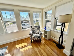 Ein Zimmer mit einem gemusterten Sessel, einem kleinen Tisch mit einer Vase und einer Stehlampe.
