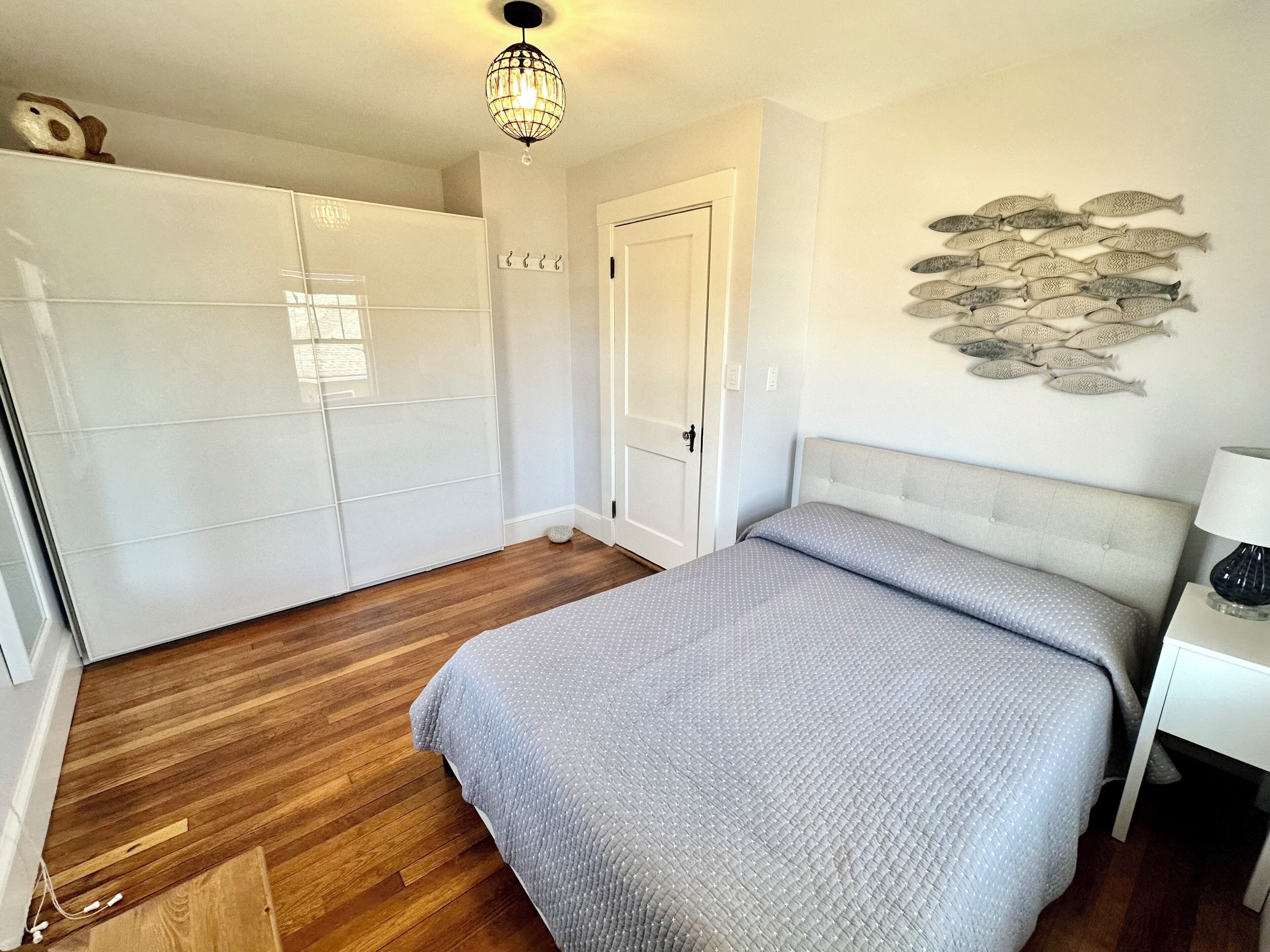 Een slaapkamer met een bed, houten vloeren, een kledingkast, een deur, een visdecoratie aan de muur en een plafondlamp.