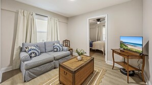 Una sala de estar con un sofá, una mesa de centro, una televisión y vista a la playa.