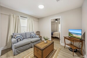 Ein Wohnzimmer mit einer Couch, einem Couchtisch, einem Fernseher und Blick auf den Strand.