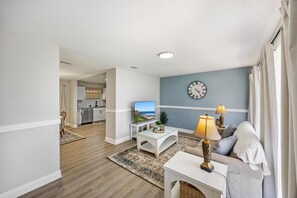 Ein Wohnzimmer mit einer Couch, einem Couchtisch, einem Fernseher und einer Uhr an der Wand.