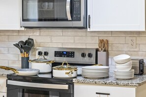 Una cocina con microondas, estufa, ollas y platos apilados.