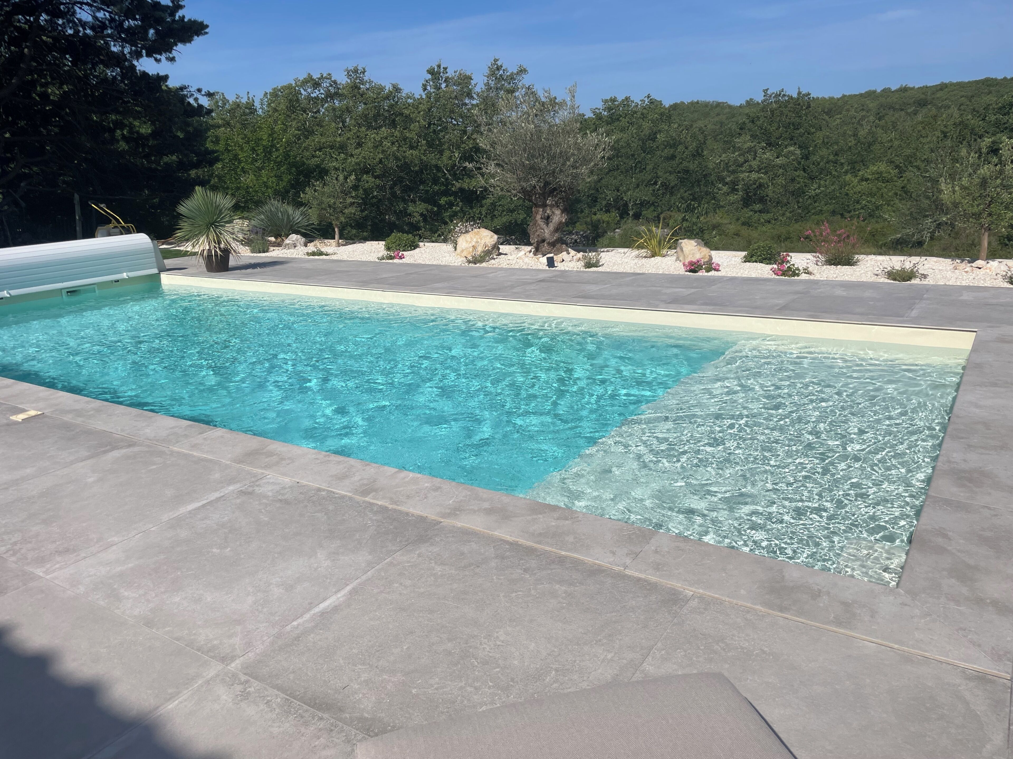 A rectangular swimming pool with clear water, surrounded by a stone deck.