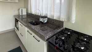 A kitchen with a granite countertop, a sink, a stove, and a window with curtains. - Cozy house with 2 air-conditioned bedrooms. (Nova Mutum)