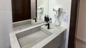 A bathroom with a large sink, a mirror, and two hair dryers mounted on the wall. - Cozy house with 2 air-conditioned bedrooms. (Nova Mutum)