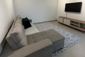 Una sala de estar con sofá, reposapiés y un televisor de pantalla plana montado en la pared.