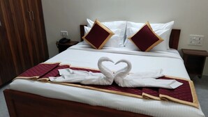Una cama bien hecha con una toalla dispuesta en forma de corazón, un armario de madera y una mesita de noche con un teléfono.