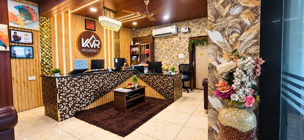 A reception area with a wooden desk, a chandelier, and a wall-mounted air conditioner. - Hotel Kvr Residency Tada  (Tada)
