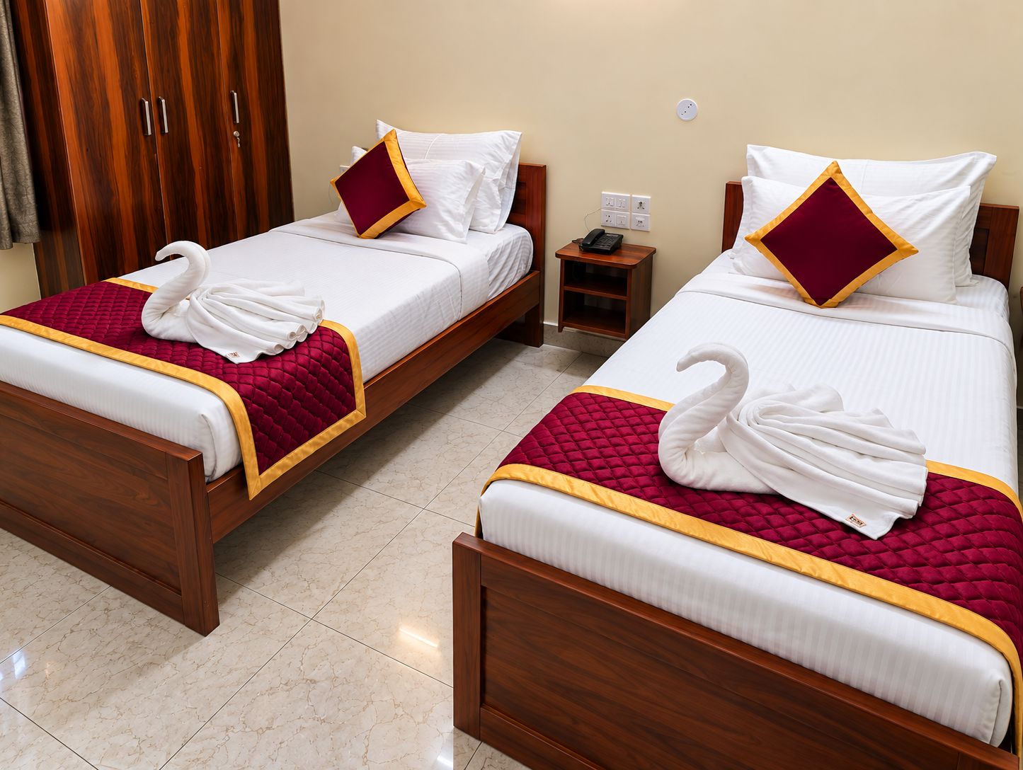 Two double beds with white linens, red and gold bedspreads, and decorative swan towels.