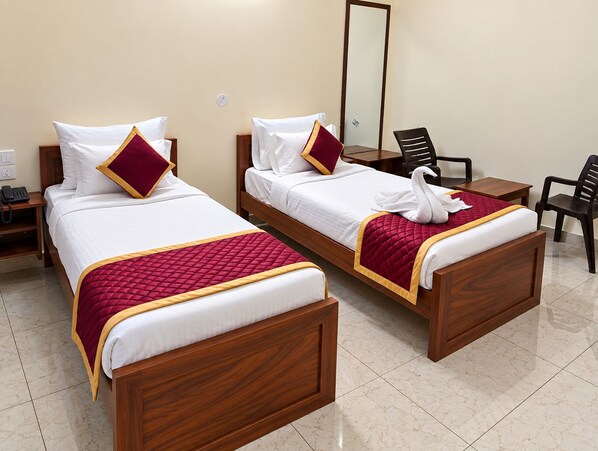 Two wooden beds with white linens and red accents, a small desk, a chair, and a mirror on the wall.