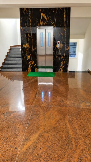 A polished granite floor leading to a staircase with a black marble wall and a metallic elevator. - Hotel Kvr Residency Tada  (Tada)