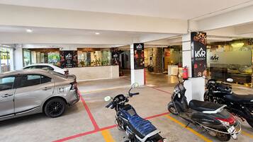 A parking area with a car and two scooters, a reception desk, and a restaurant with a sign for VVR Residency.