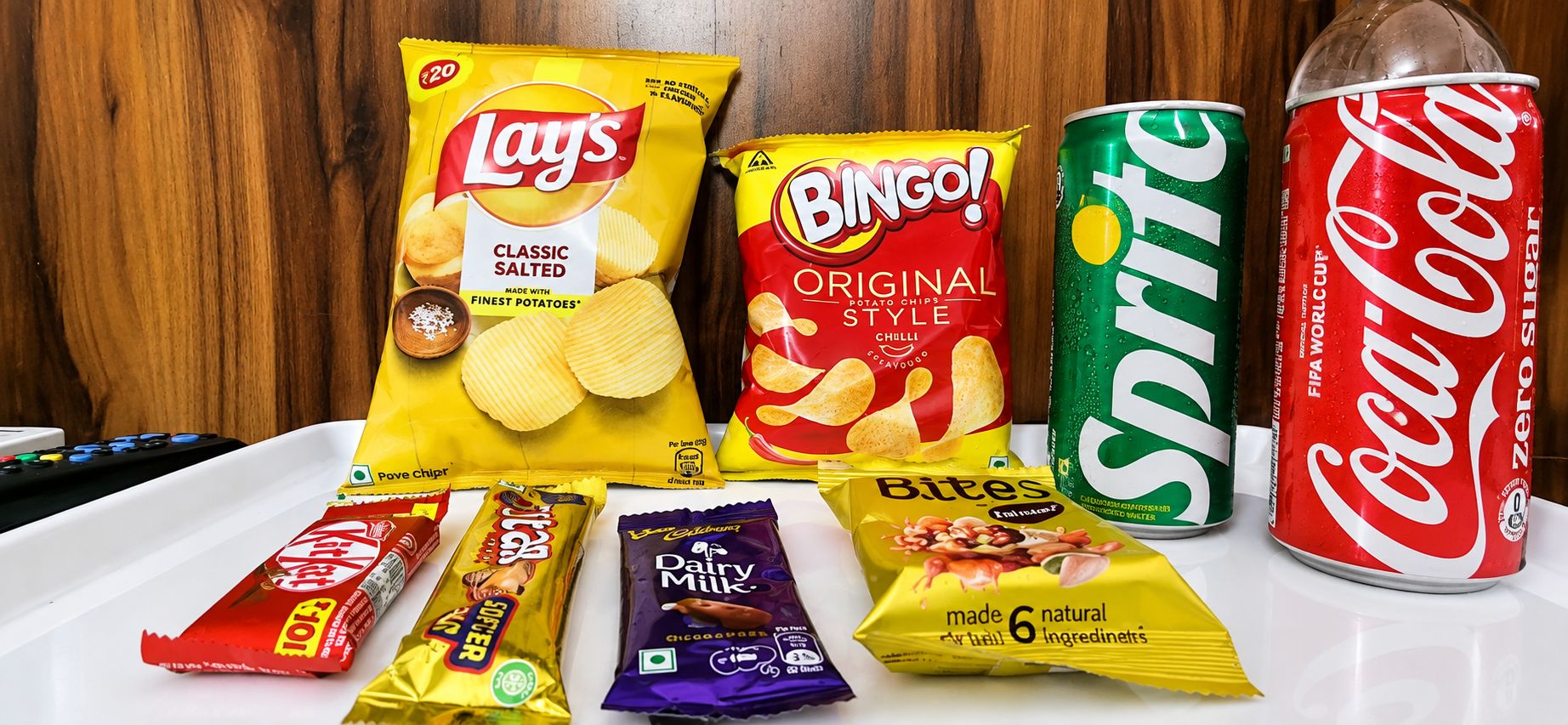 A variety of snacks and beverages including Lay's Classic Salted Potato Chips, Bingo! Original Style Potato Chips, Sprite, Coca-Cola Zero Sugar, KitKat, Cadbury Dairy Milk, and Bites.
